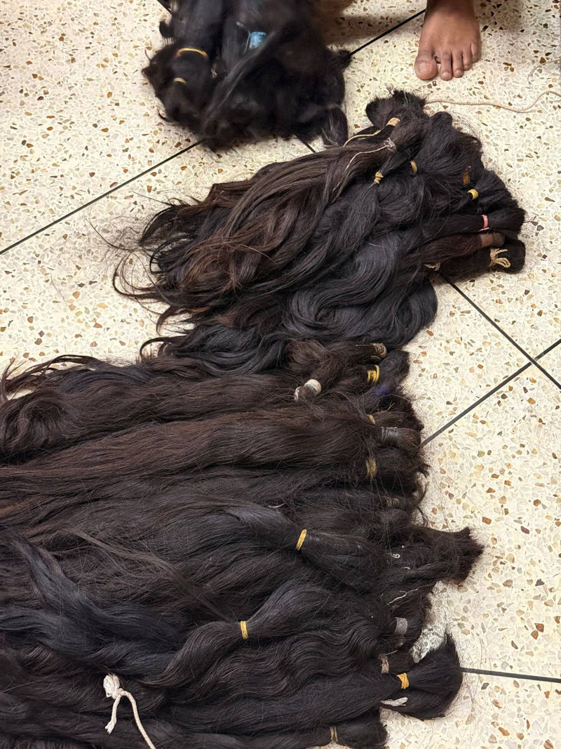 Bulk raw hair extensions displayed on the floor, showcasing different textures and bundles.