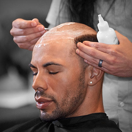 Person getting hair treatment or styling with a product on a bald head.