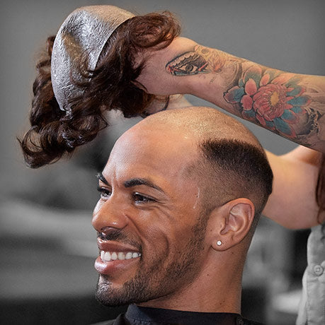 Person getting a hair style with a ponytail on a man's head.